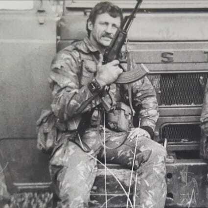 Mike West with rifle, vehicle in background